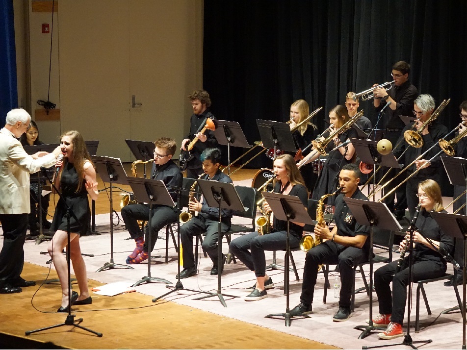 The Kalamazoo College Jazz Ensemble all dressed in black, performing with a singer front and center.